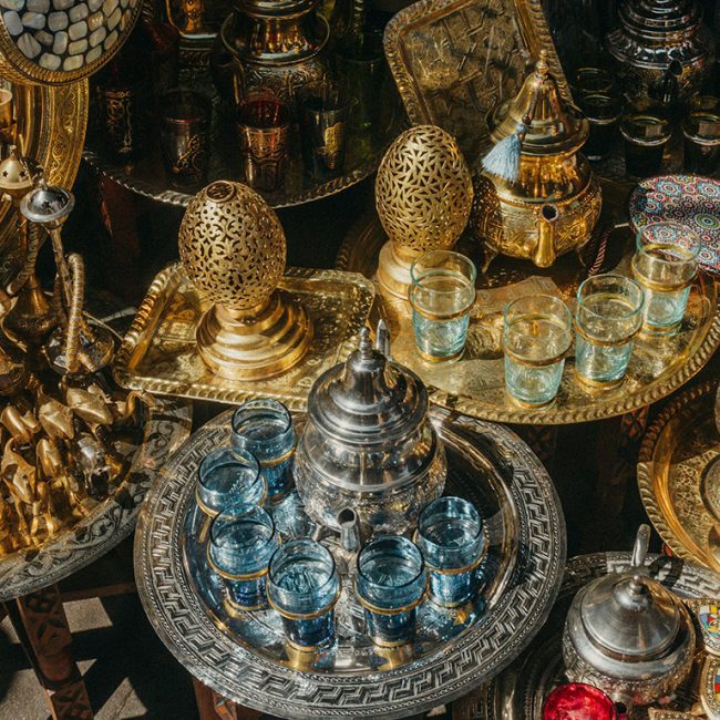Ensemble d'objets artisanaux marocains comprenant une théière traditionnelle en métal ciselé, des plateaux en cuivre finement décorés, et des verres à thé, illustrant l'élégance et le savoir-faire de l'artisanat marocain.