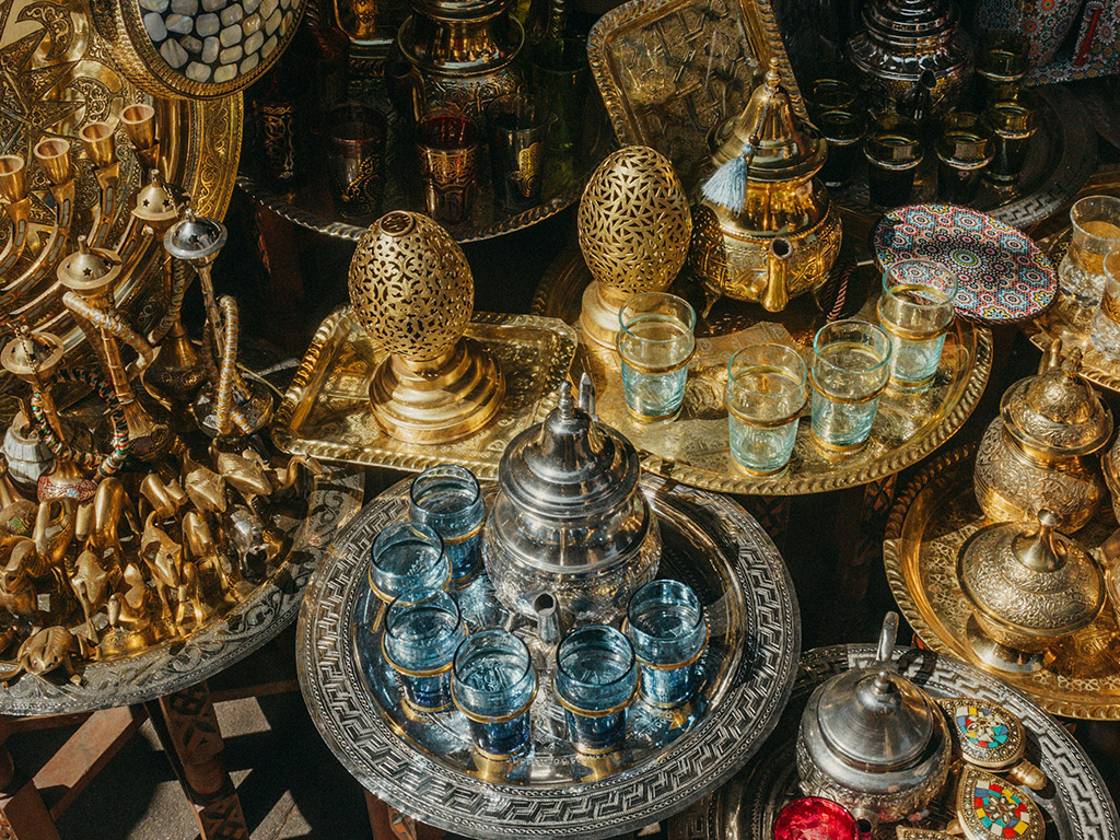 Ensemble d'objets artisanaux marocains comprenant une théière traditionnelle en métal ciselé, des plateaux en cuivre finement décorés, et des verres à thé, illustrant l'élégance et le savoir-faire de l'artisanat marocain.
